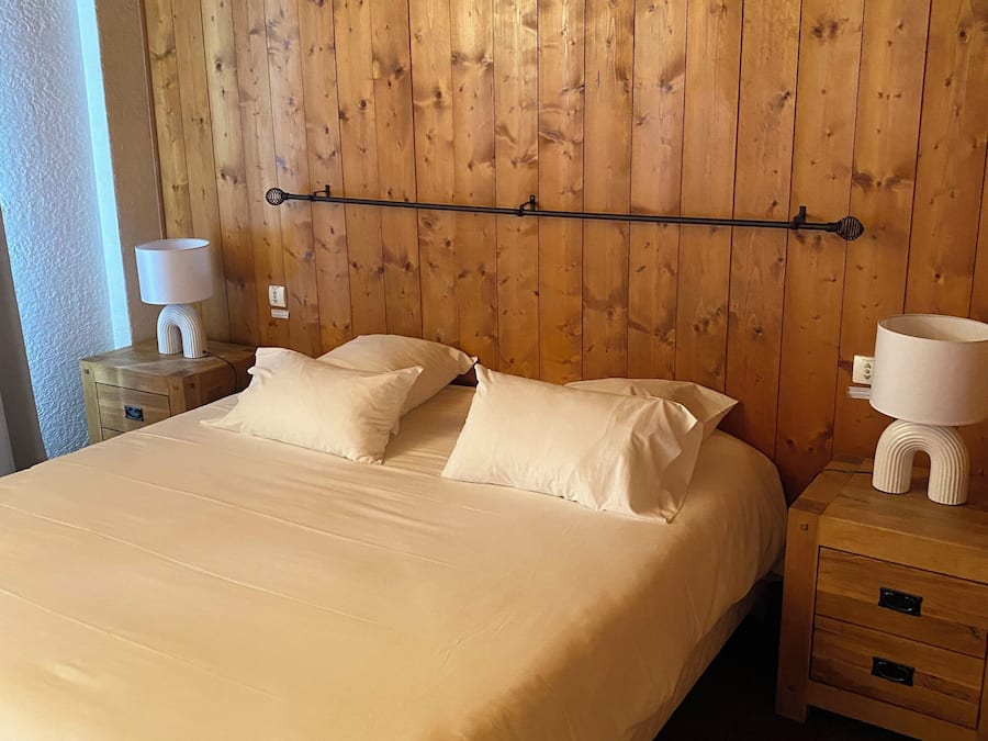 Un dormitorio con cabecera de madera, una cama grande con sábanas blancas, dos mesitas de noche con lámparas y una cómoda con cajones.