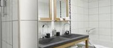 A modern bathroom with white tiles, a wooden vanity, a double mirror, and a shower area.