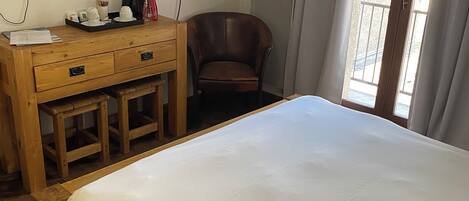A hotel room with a bed, a wooden desk with a chair, a television, and a window with curtains.