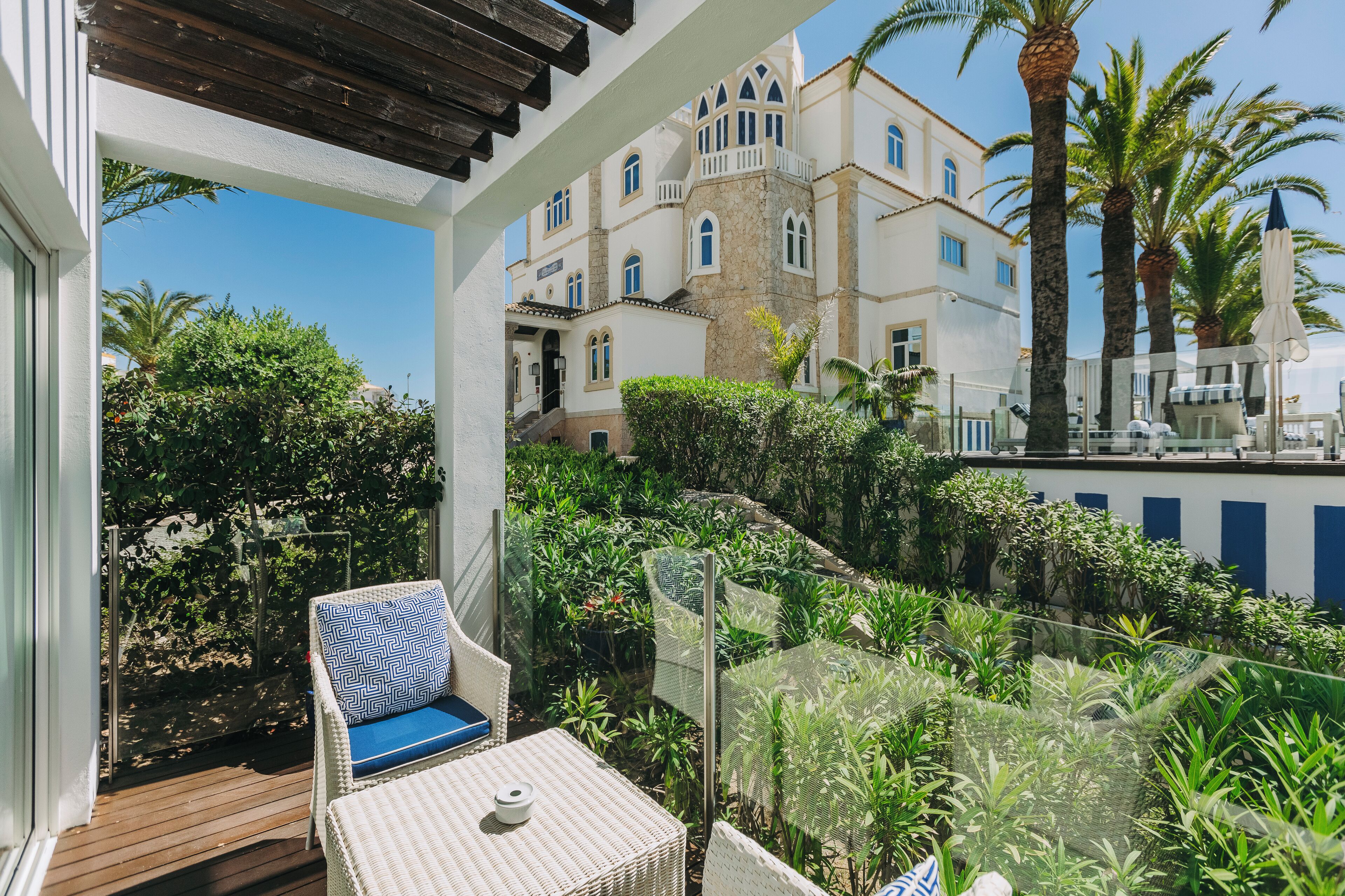 A balcony with wicker furniture, a view of a building with multiple windows, and lush greenery.