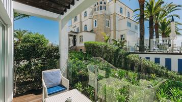A balcony with wicker furniture, a view of a building with multiple windows, and lush greenery.