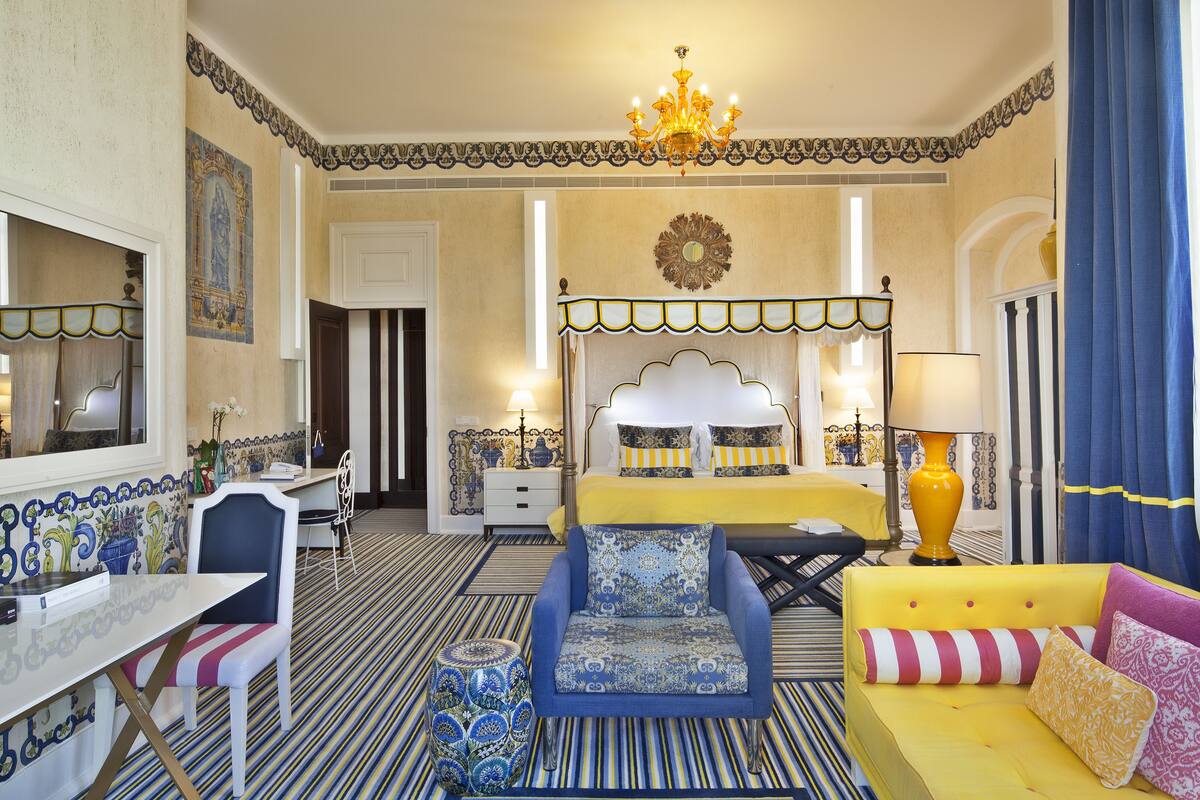 A hotel room with a bed, a sofa, a chair, a table, and a lamp.