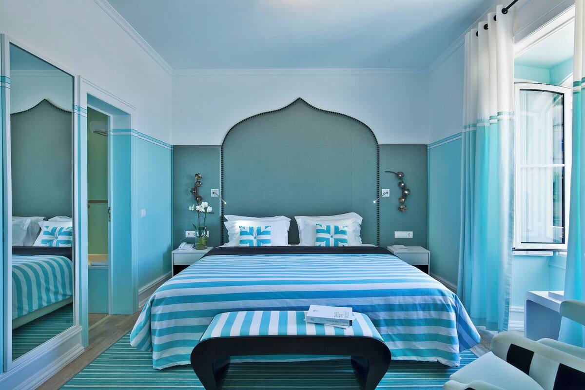 A hotel room with a large bed, a bedside table, a chair, and a window with curtains.