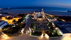 An aerial view of a coastal hotel with a central building, a beach, and a parking area.