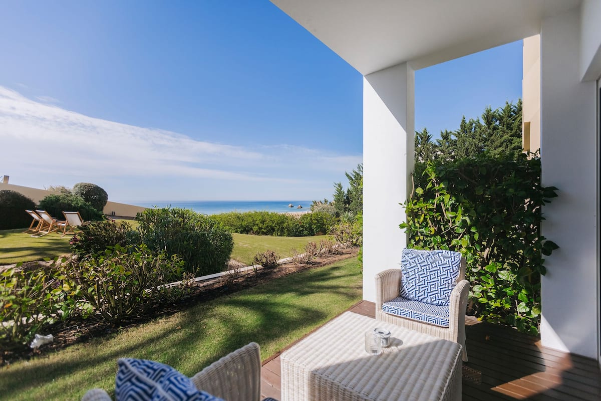 A patio with wicker furniture, a view of the sea, and a well-maintained garden.