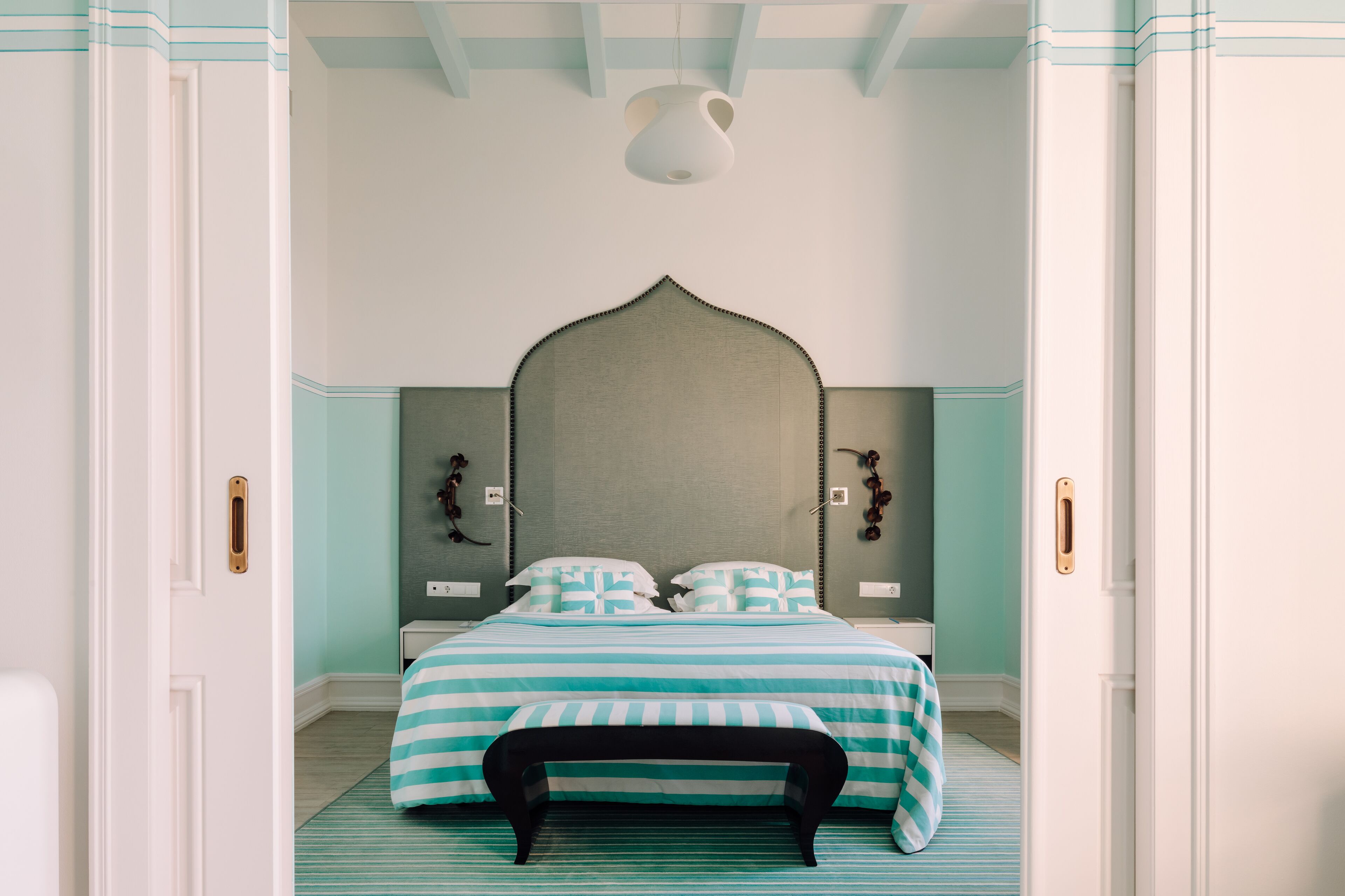 A bedroom with a bed, a bench, a bedside table, and a wall-mounted light fixture.