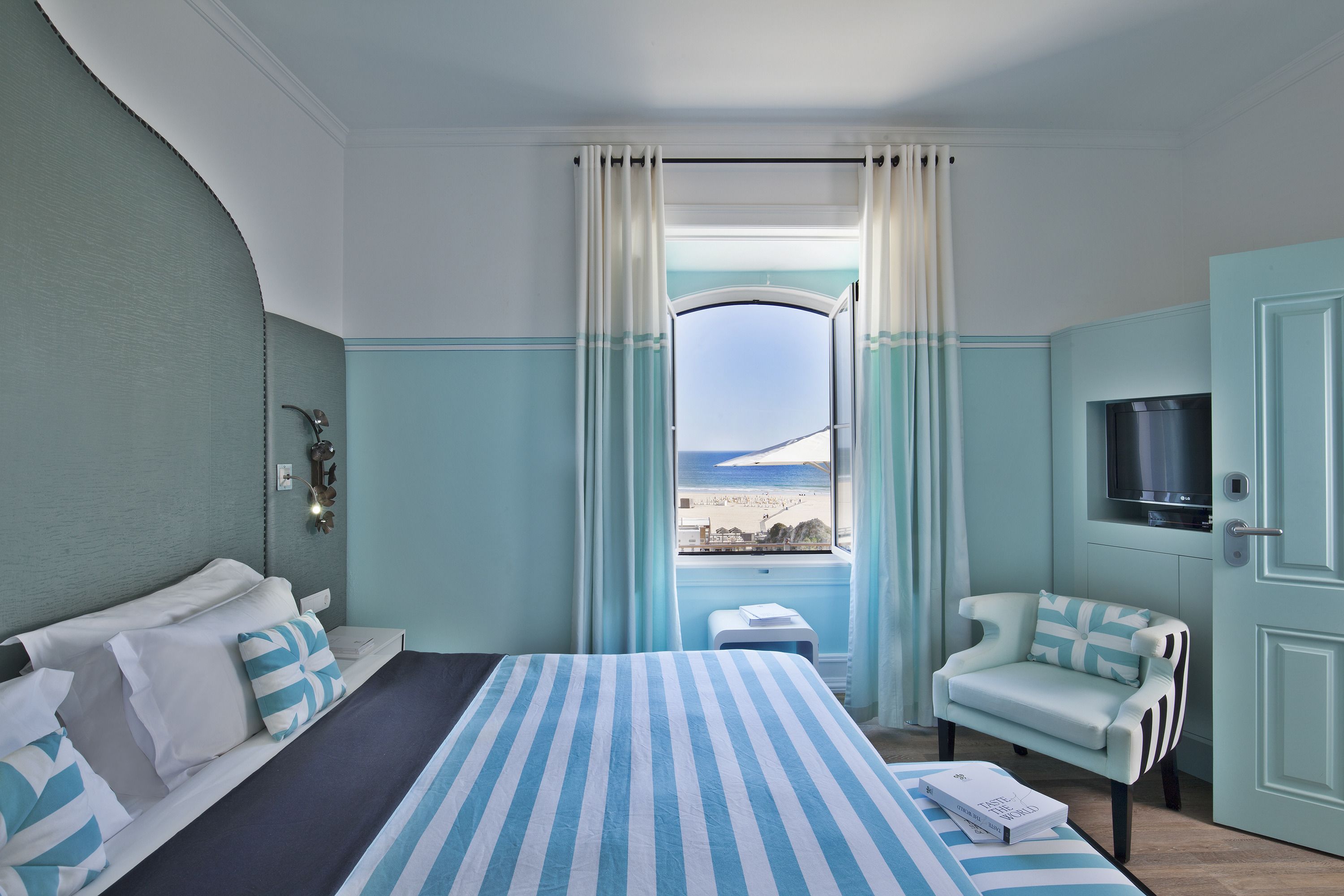 Ein Hotelzimmer mit Bett, Sessel, Fernseher und einem Fenster mit Meerblick.