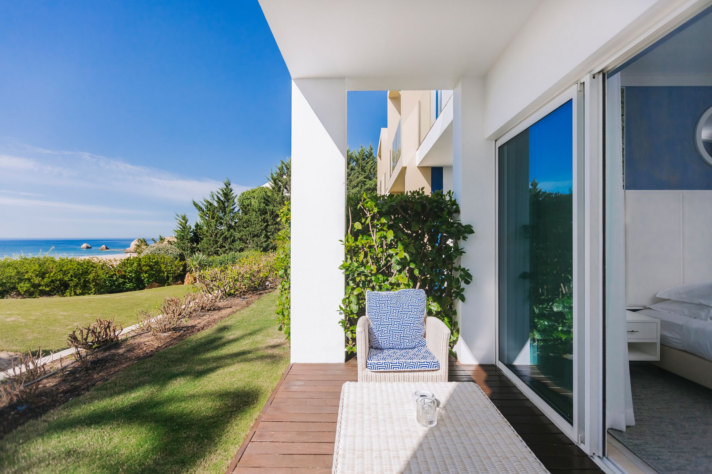 Un patio moderno al aire libre con vista al océano, una silla de mimbre con cojín estampado y una mesa de vidrio.