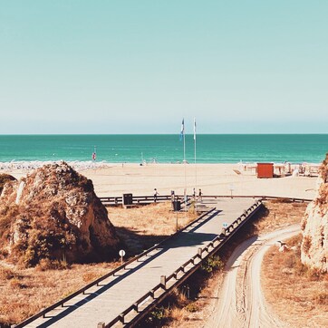 A coastal walkway leading to a beach with a clear view of the ocean.