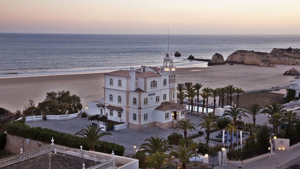 A coastal building with a prominent tower, adjacent to a beach and palm trees.