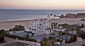 A coastal building with a prominent tower, adjacent to a beach and palm trees. - Bela Vista Hotel & SPA - Relais & Châteaux (Portimão)