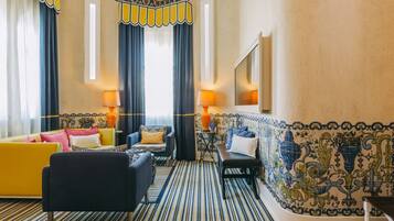 A hotel room with striped carpet, a yellow sofa, a blue armchair, a black bench, and a tiled wall with decorative patterns.