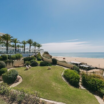 A coastal hotel with a large lawn, palm trees, and a beach view.