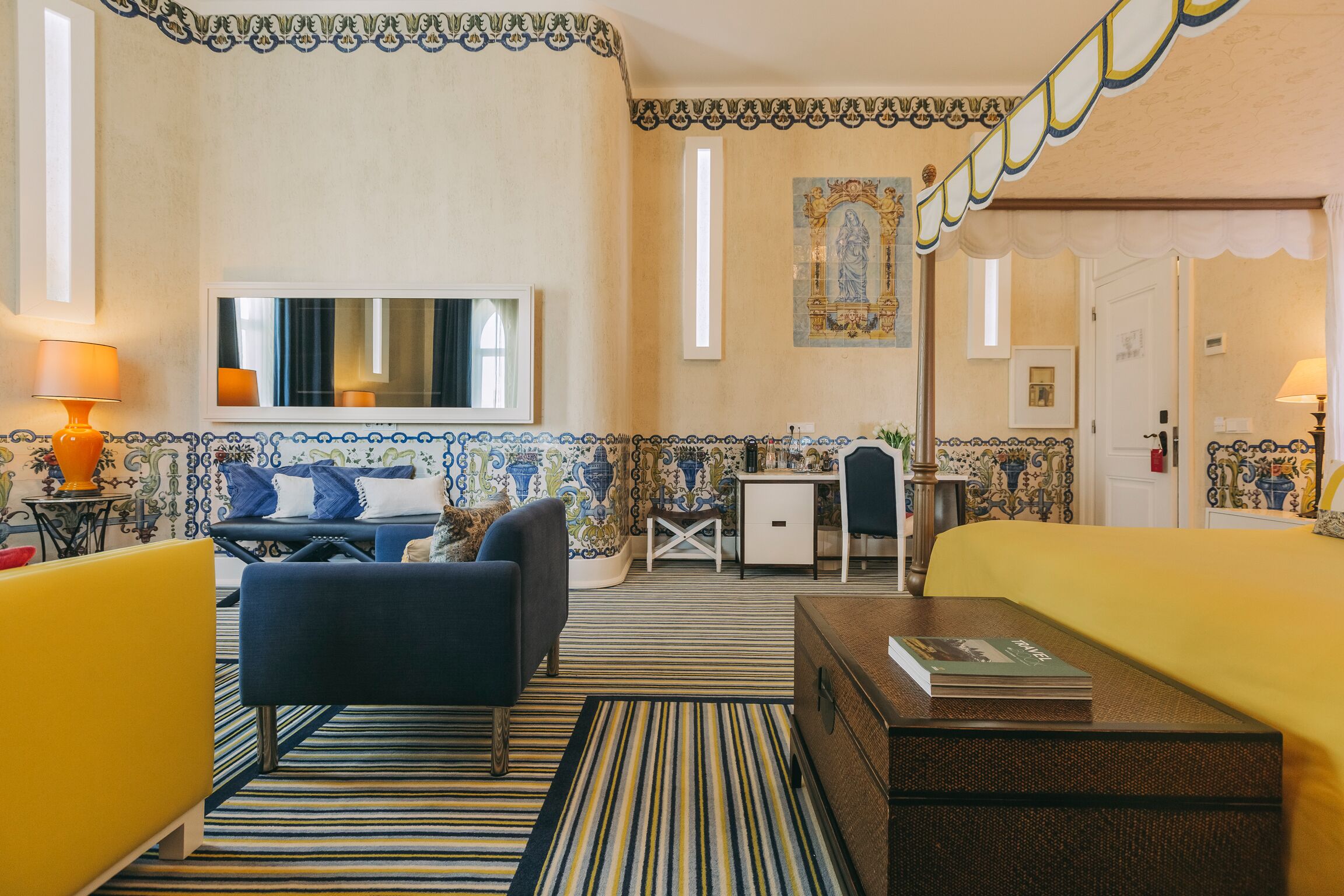 A hotel room with a striped carpet, a sofa, a small table, a desk, and a bed.