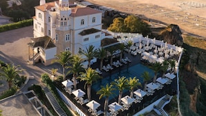 A coastal hotel with a large pool area, a beach view, and a prominent building with a tower.