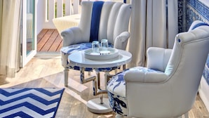 A balcony with a view of the ocean, a white armchair, a round table with a tray, and a floor lamp.