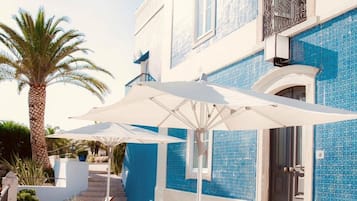 Een gebouw met blauw betegelde buitenmuren, een balkon met versierde reling en buitenzitplaatsen met parasols.