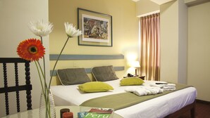 A hotel room with a bed, pillows, a table with a book, a vase with flowers, and a painting on the wall. - Hotel Kamana (Lima)