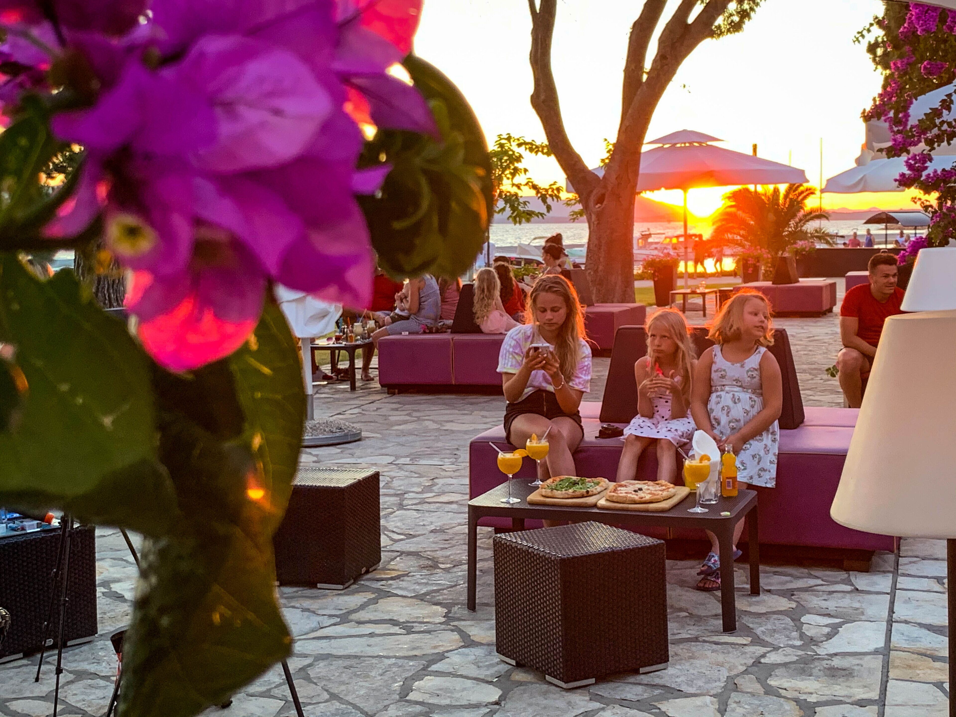 An outdoor seating area with stone flooring, wicker furniture, and a view of the sunset over the water.