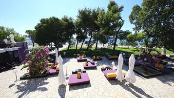 An outdoor seating area with stone flooring, cushioned seating, and umbrellas.