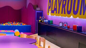 A playroom with a ball pit, a table, chairs, and a wall with the word "PLAYROOM" in large letters.