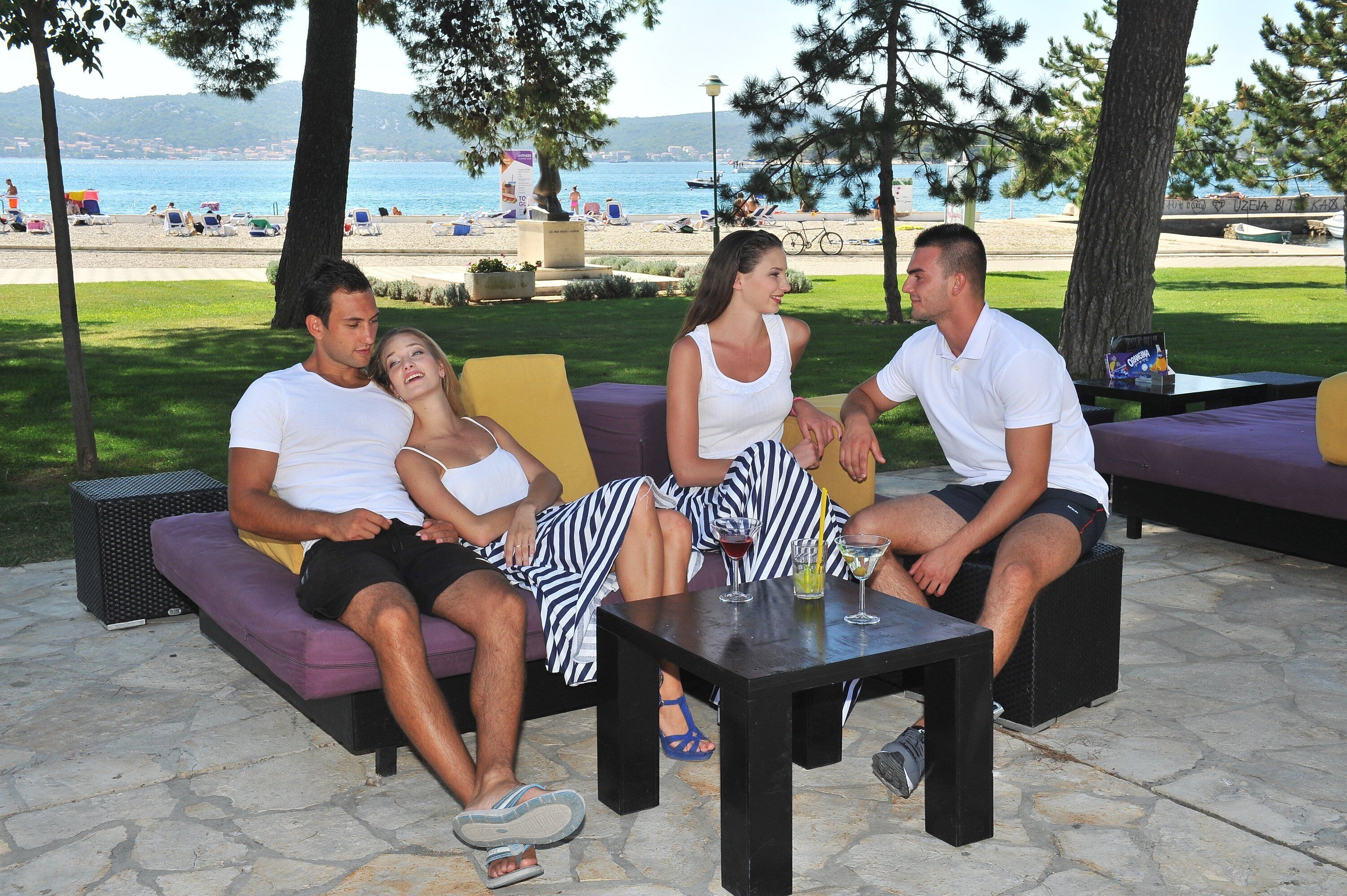 A group of people sitting on outdoor furniture by a beach, with a table in front of them.