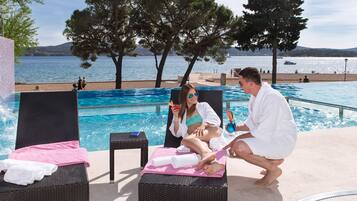 A poolside area with lounge chairs, a pool, and a view of the sea.