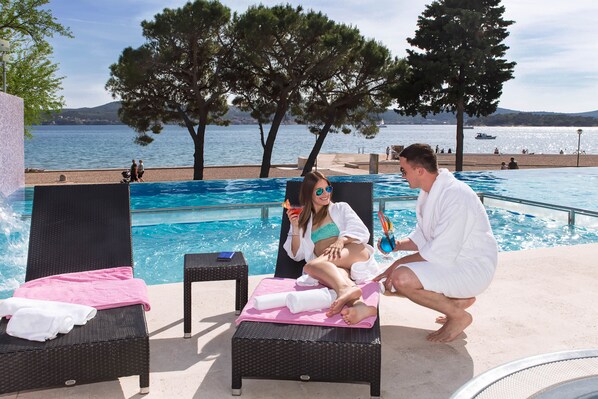 A poolside area with lounge chairs, a pool, and a view of the sea.