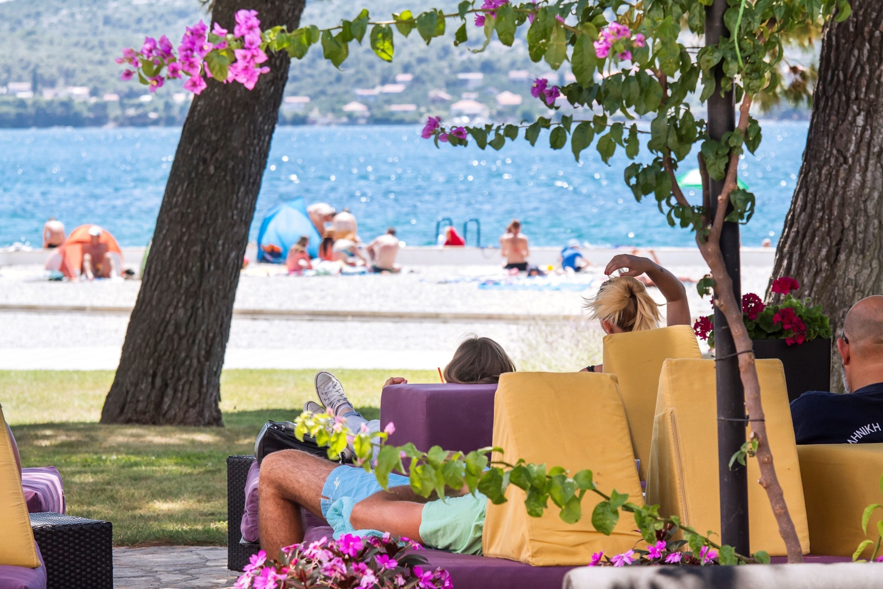 Un salón junto a la playa con asientos al aire libre, con vistas a una playa con gente y sombrillas.