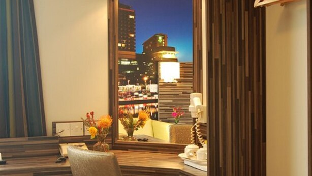 A hotel room with a desk, chair, and a vase with flowers. There is a large window with a view of a cityscape at night. - B&B Hotel Manchester SportCity (Manchester)