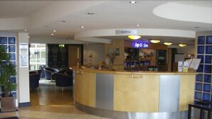 A hotel reception area with a curved counter, a reception desk, and a bar area. - B&B Hotel Manchester SportCity (Manchester)