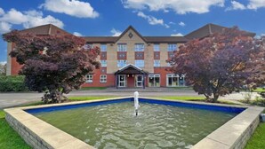 A hotel with a swimming pool in front, surrounded by trees and a clear blue sky. - B&B Hotel Manchester SportCity (Manchester)