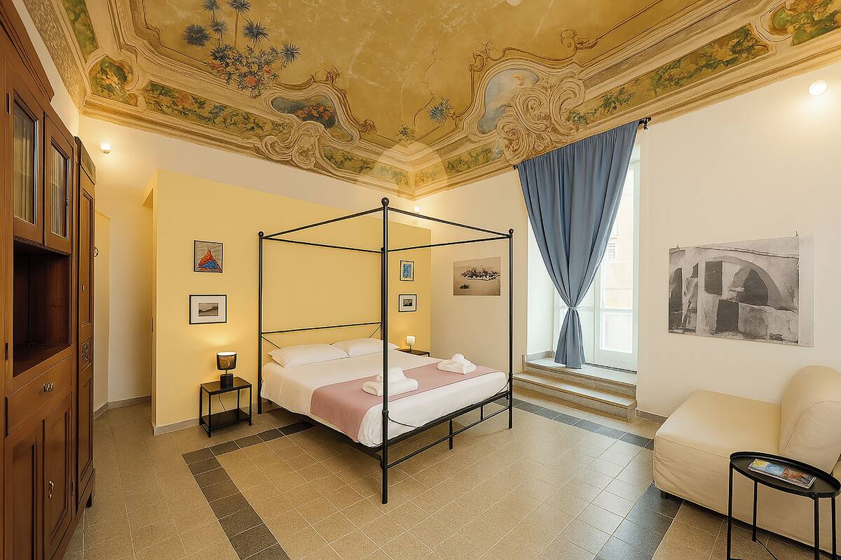 A four-poster bed with a nightstand, a chair, and artwork on the walls.