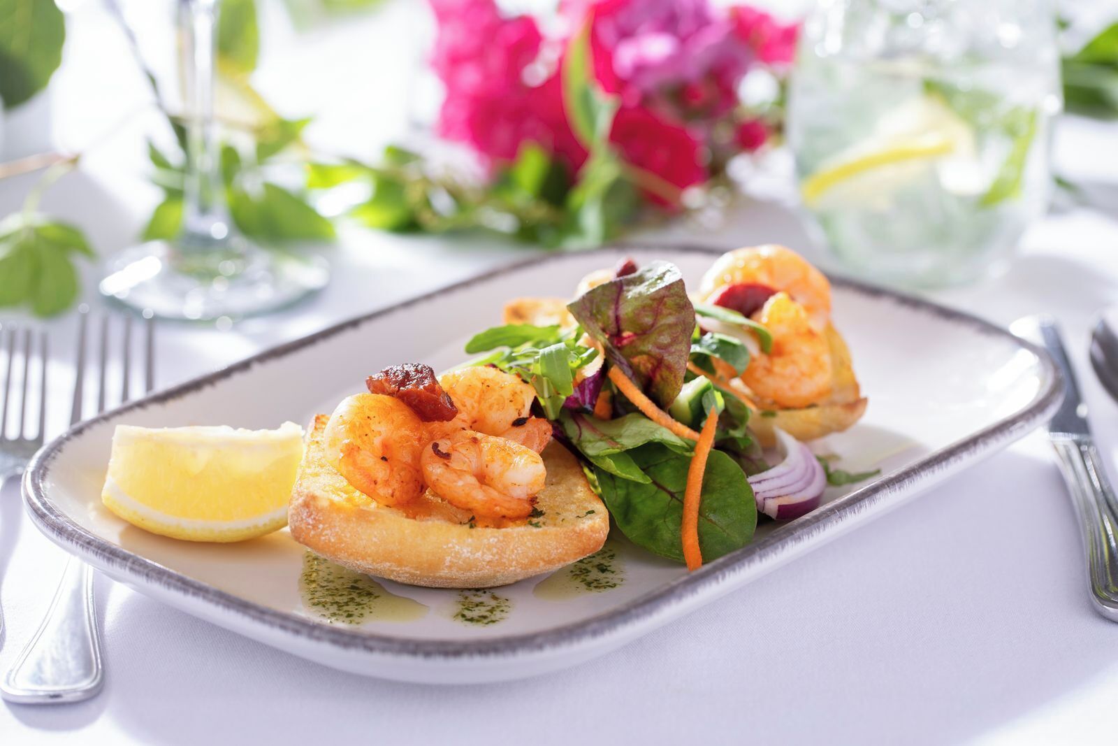 A plate of shrimp on toast with a side salad and lemon wedge.