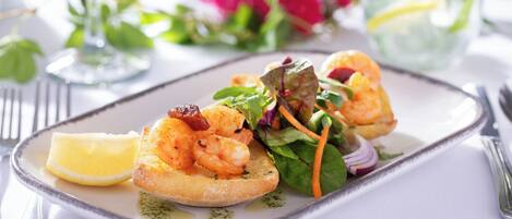A plate of shrimp on toast with a side salad and lemon wedge.