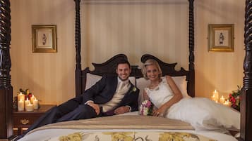 A four-poster bed with a floral bedspread, a wooden headboard, and framed pictures on the walls.