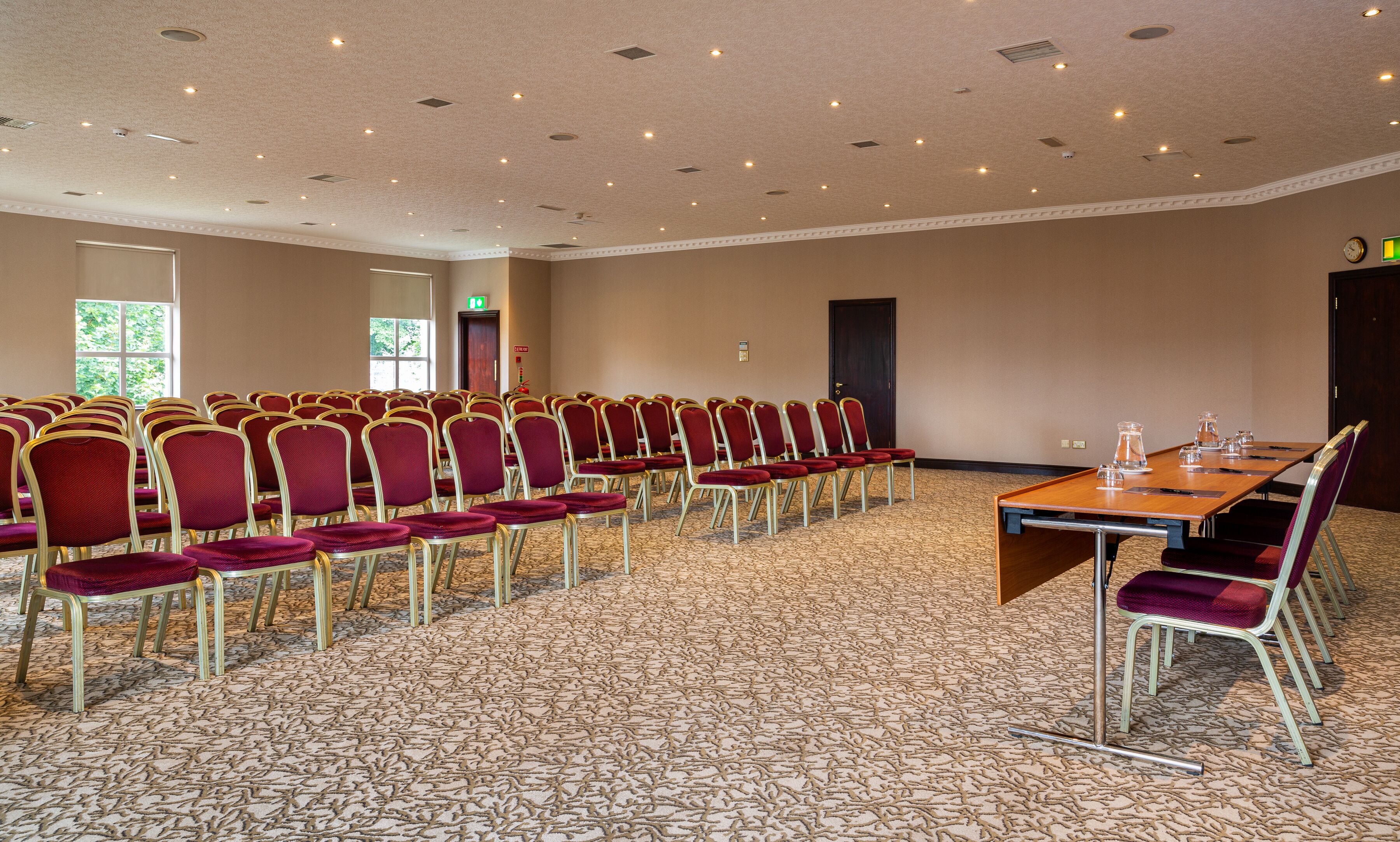 Une salle de conférence avec des rangées de chaises, une longue table, un sol recouvert de moquette et des luminaires au plafond.