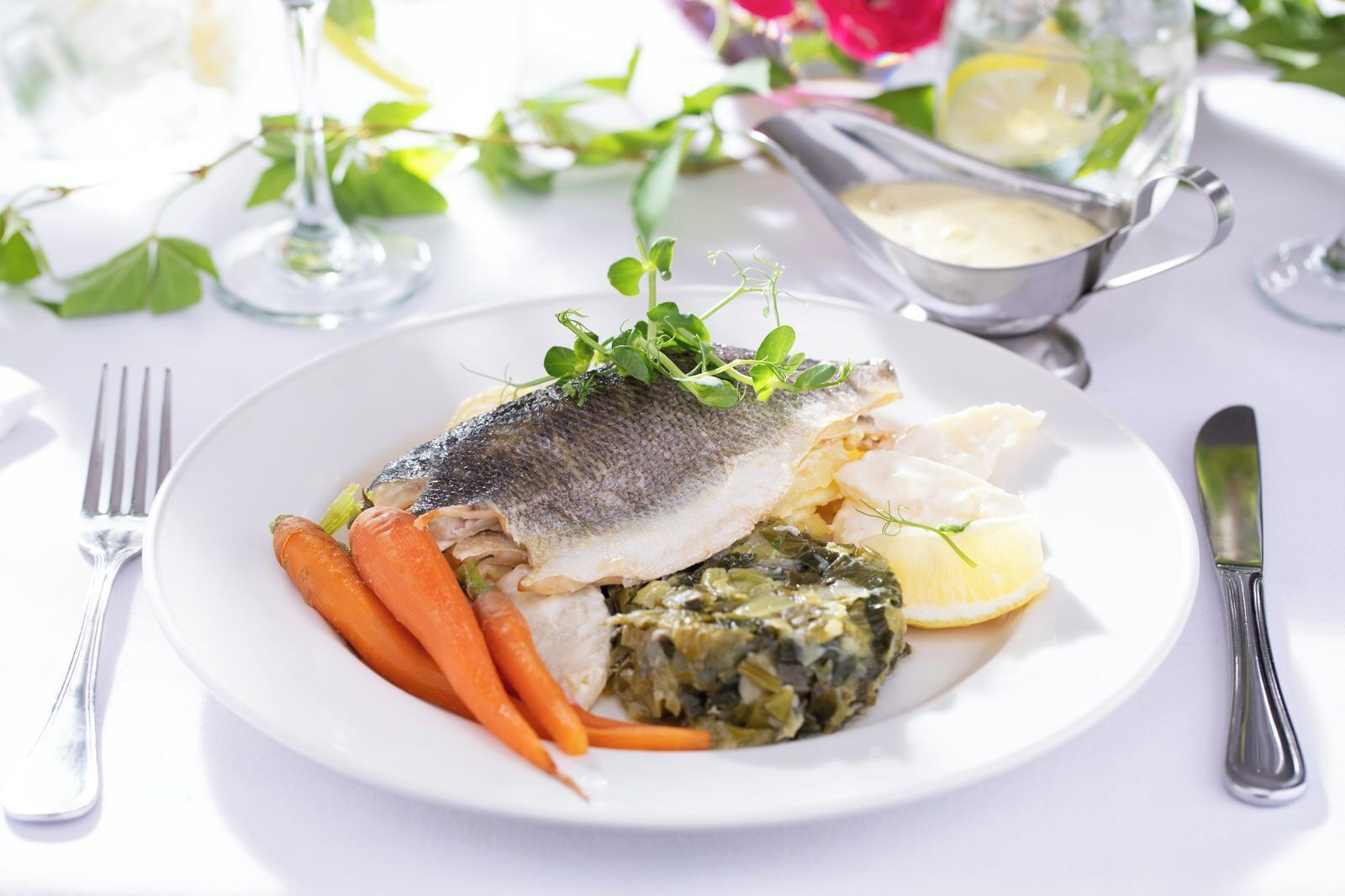 Un plato de pescado, zanahorias y verduras sobre una mesa blanca.