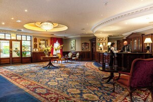 A hotel lobby with a large carpeted area, a reception desk, and a chandelier.