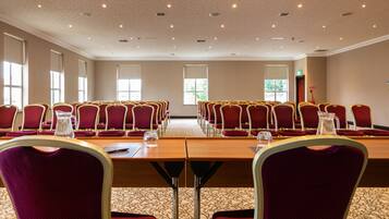 Un salón de conferencias con filas de sillas rojas, una mesa grande y luces en el techo.