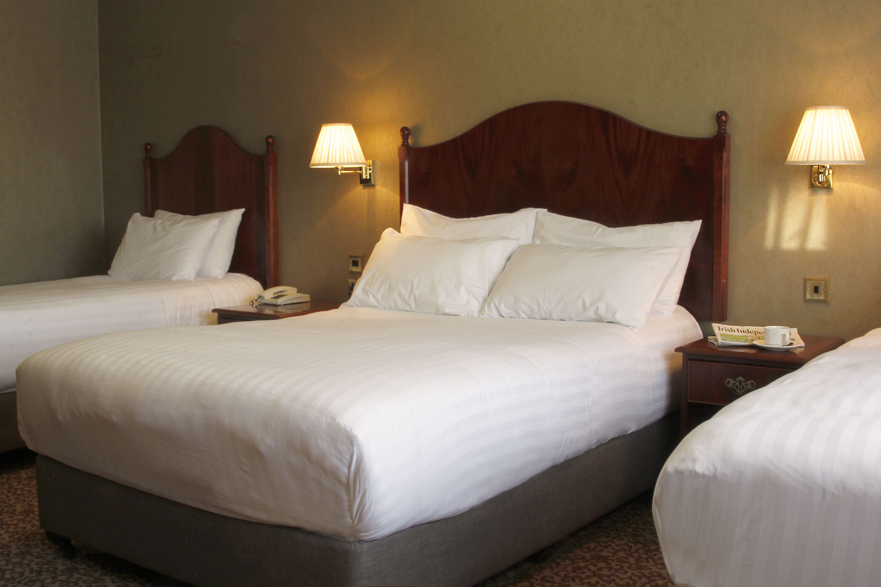 A hotel room with two single beds, each with a wooden headboard, white linens, and bedside lamps.