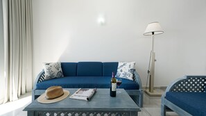 A modern living room with a blue sofa, patterned pillows, a hat, a wine bottle, and a magazine on a small table.