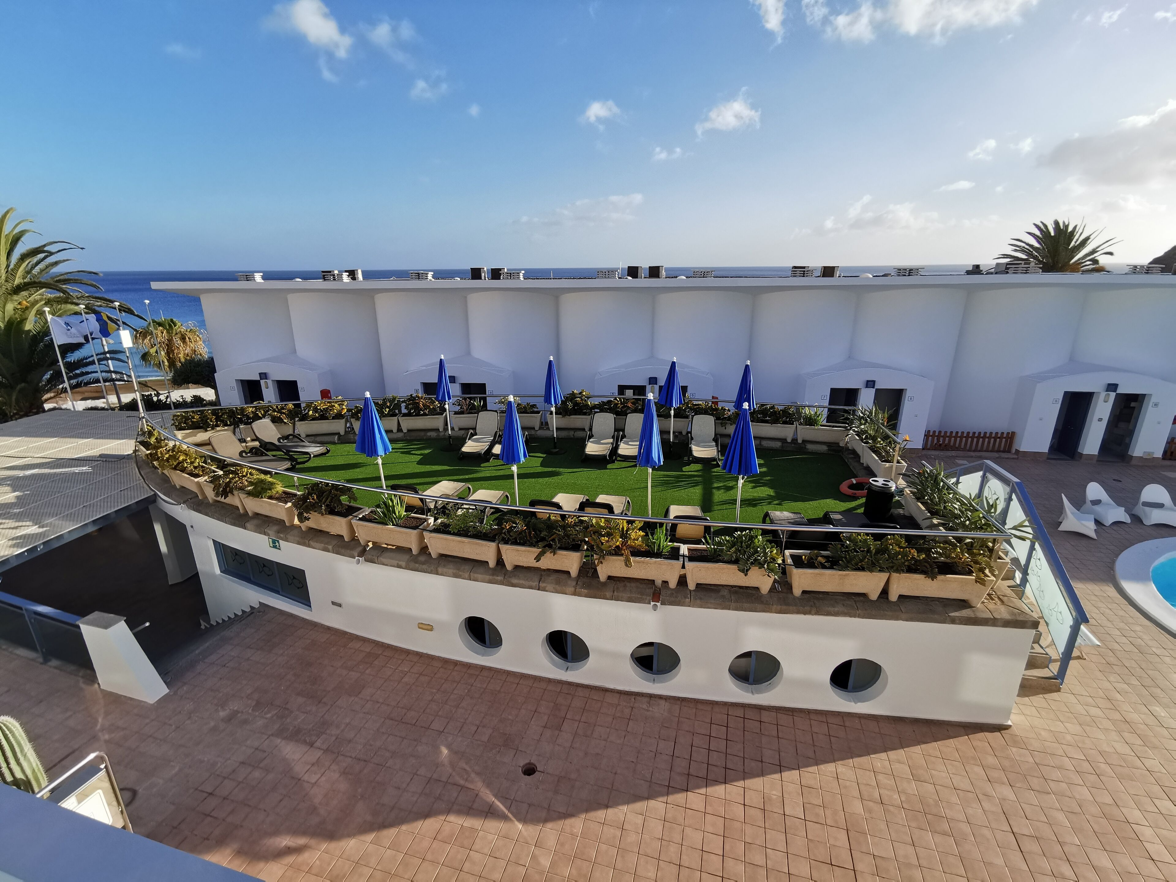 A rooftop terrace with lounge chairs, blue umbrellas, and a pool.