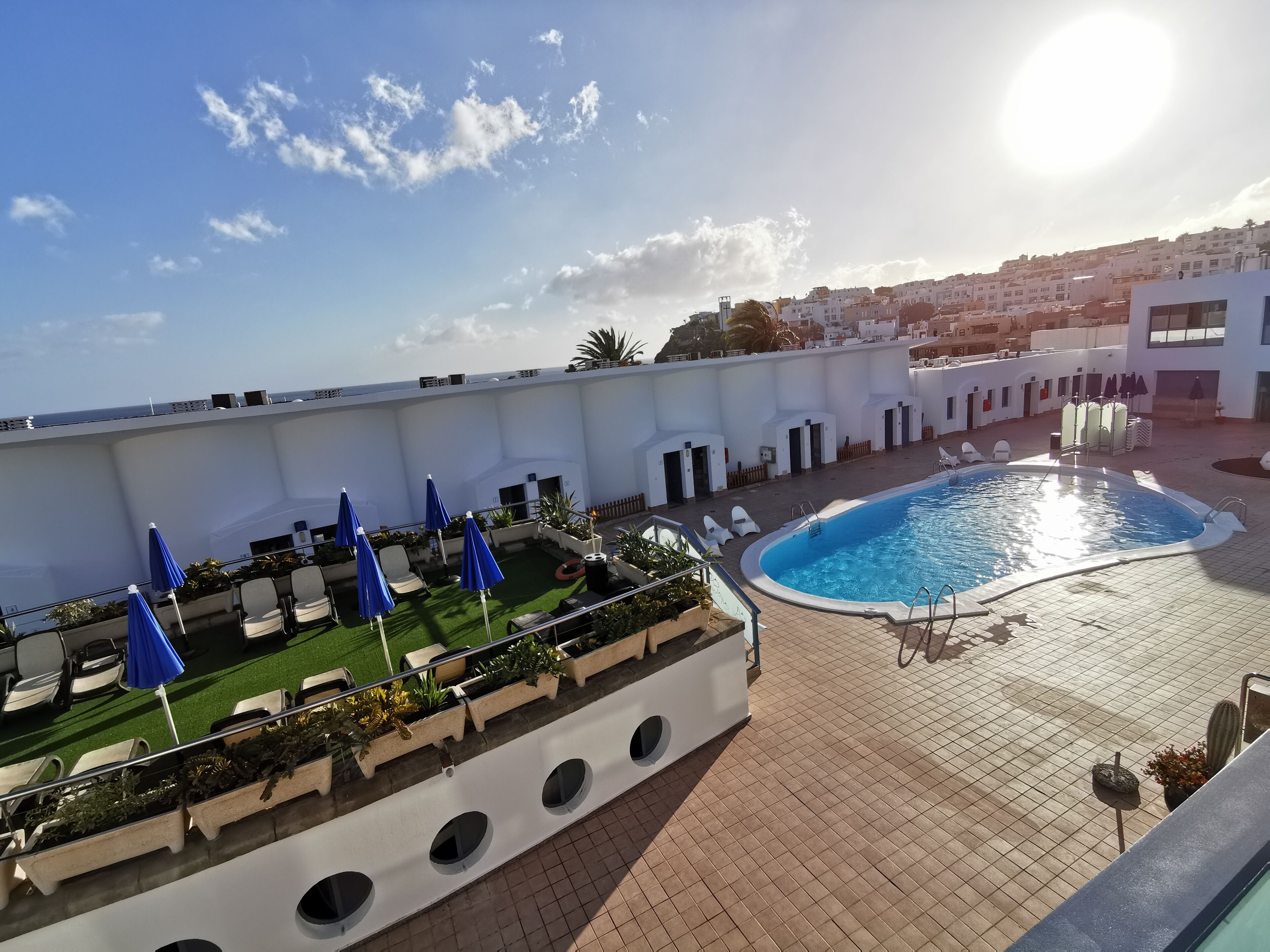 Un espace piscine aménagé sur le toit, offrant une vue dégagée sur la mer, avec des chaises longues et des parasols.