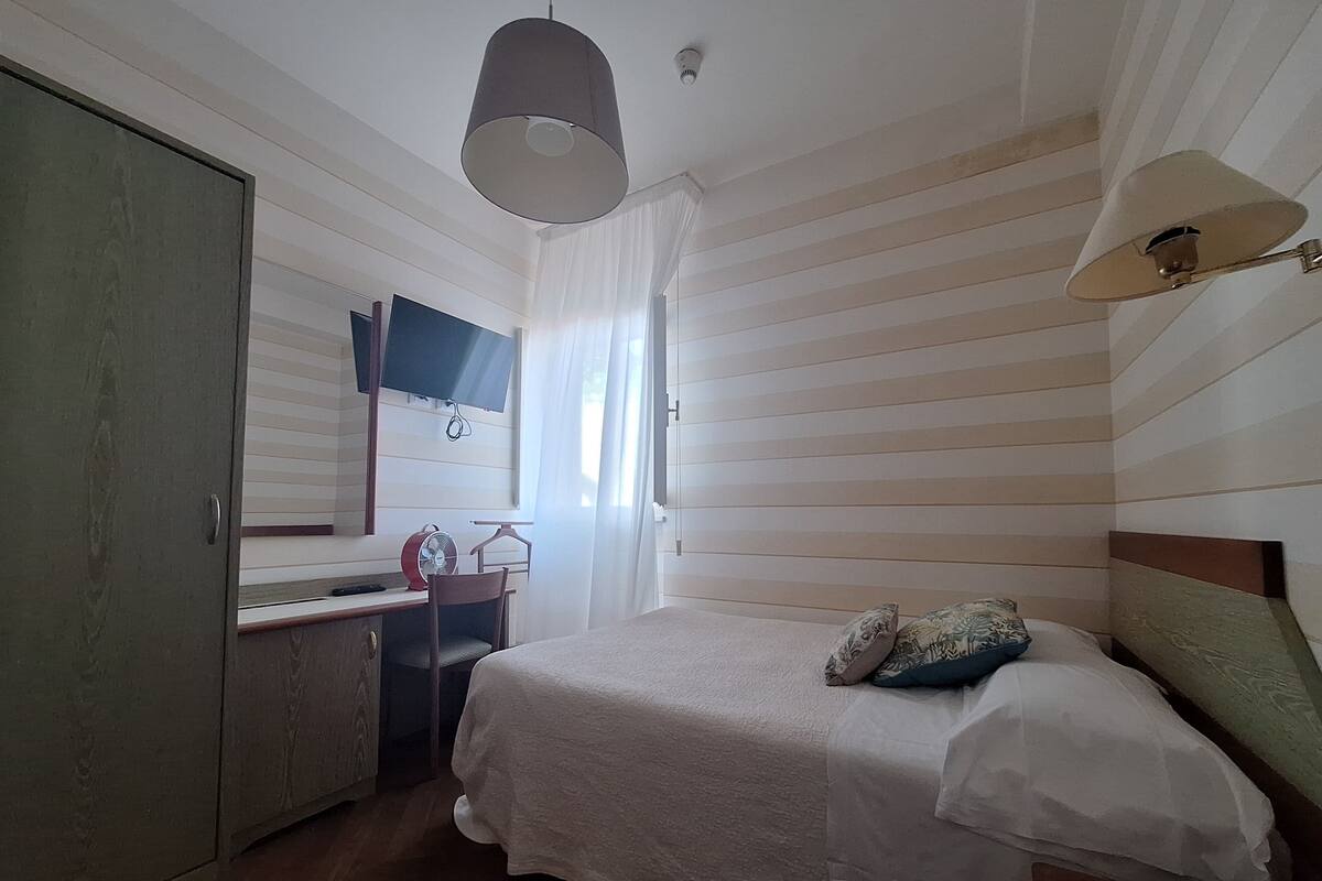 Een slaapkamer met een bed, een bureau, een stoel, een kledingkast en een televisie.