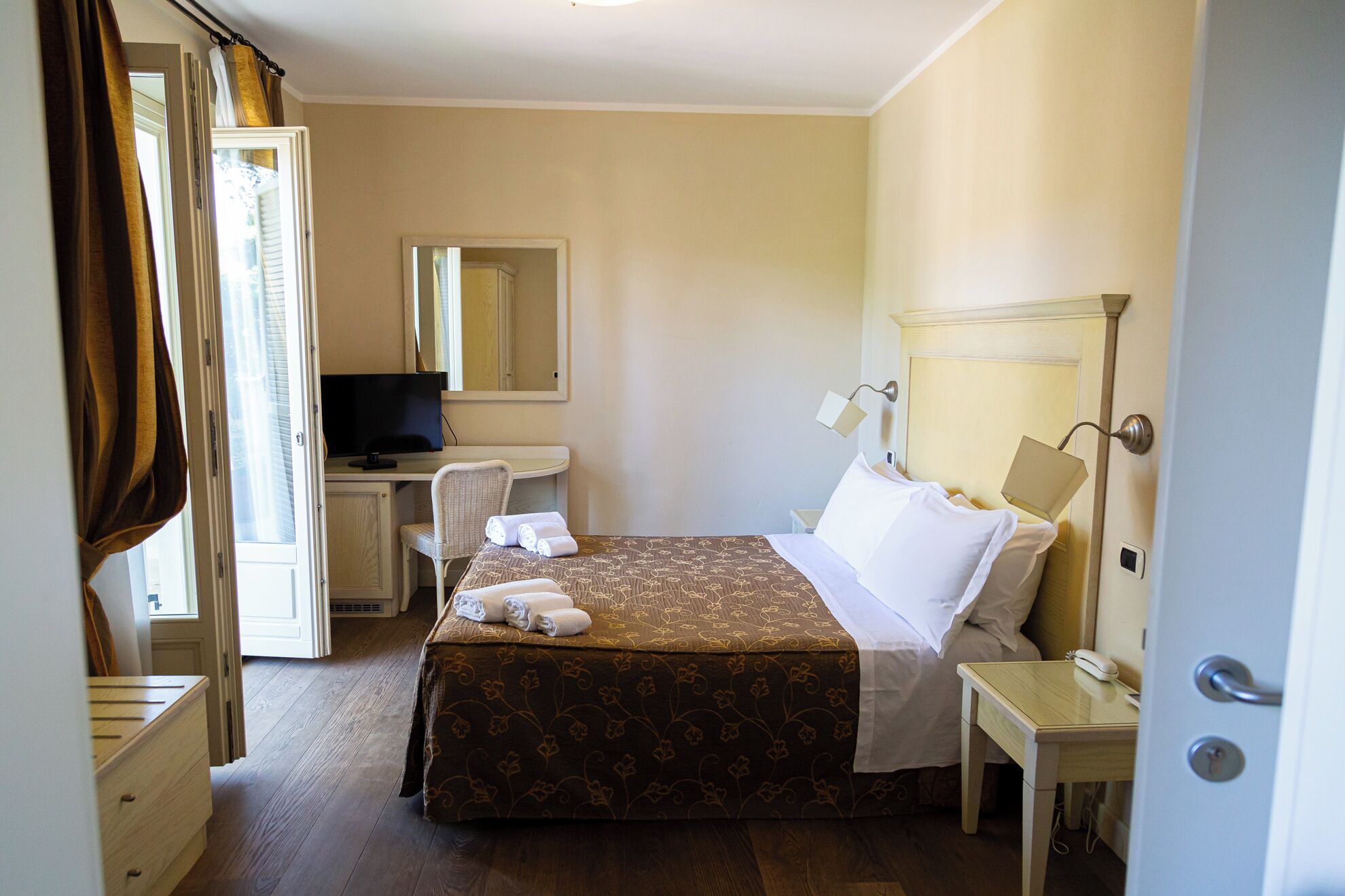 Une chambre d’hôtel comprenant un lit, un bureau avec un ordinateur, une chaise, une table de chevet et une lampe.