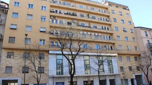 Un hotel de varios pisos con balcones, una entrada central y un cartel que indica una tienda y un ascensor.