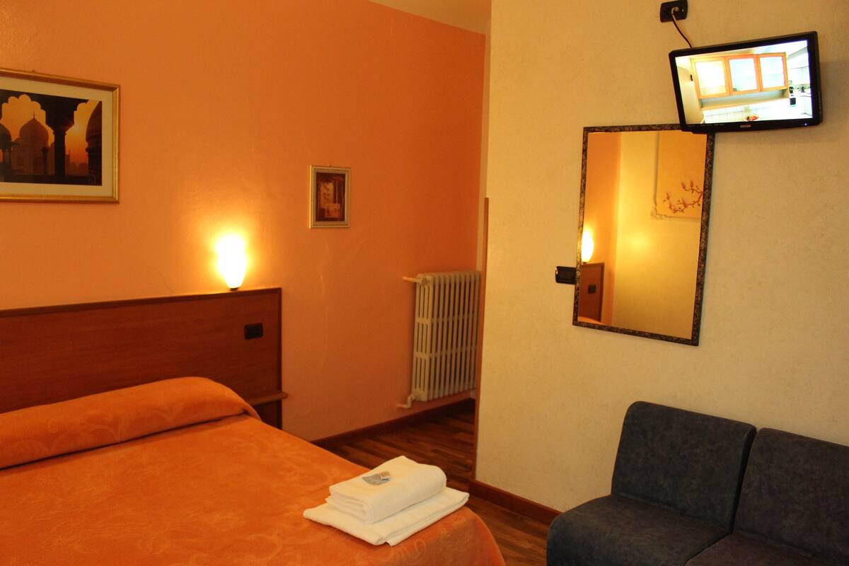 Una camera d'albergo con un letto, un divano, una TV a muro e un quadro incorniciato.