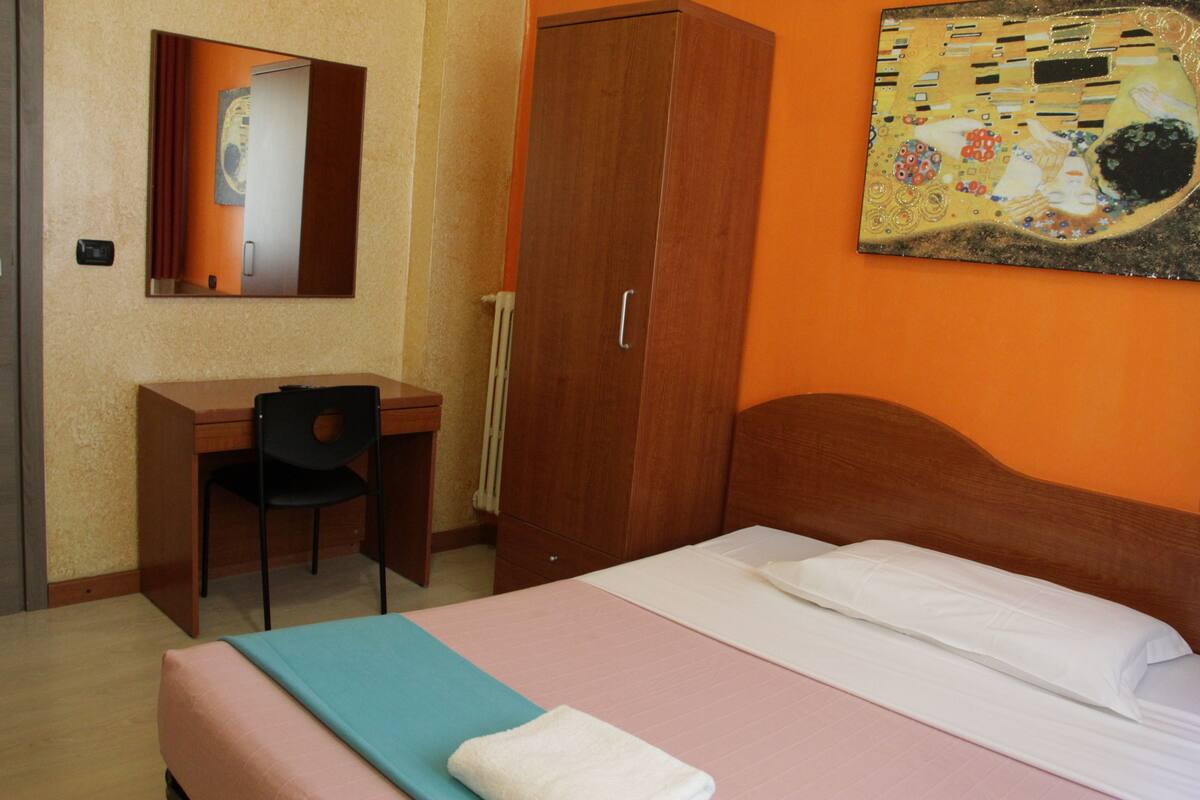 Una camera d'albergo con un letto, una scrivania, una sedia e un armadio.