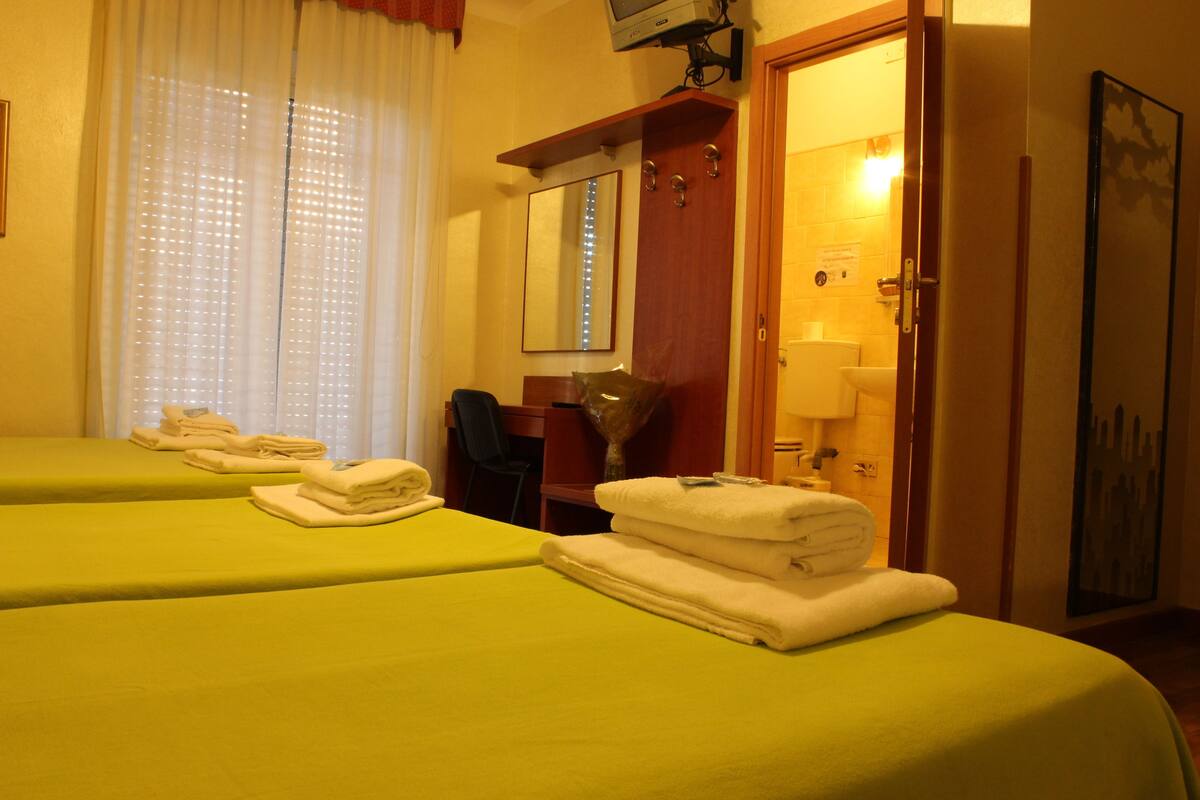 Una camera d'albergo con due letti, una scrivania, uno specchio e l'ingresso del bagno.
